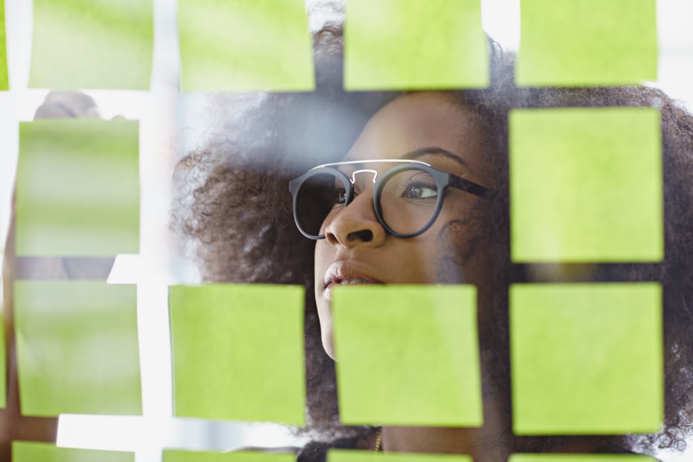 Portrait of a business woman with an afro behind sticky notes in bright glass office